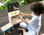 A child sitting on the ground playing with the PlanToys Workbench.