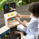 A child sitting on the ground playing with the PlanToys Workbench.