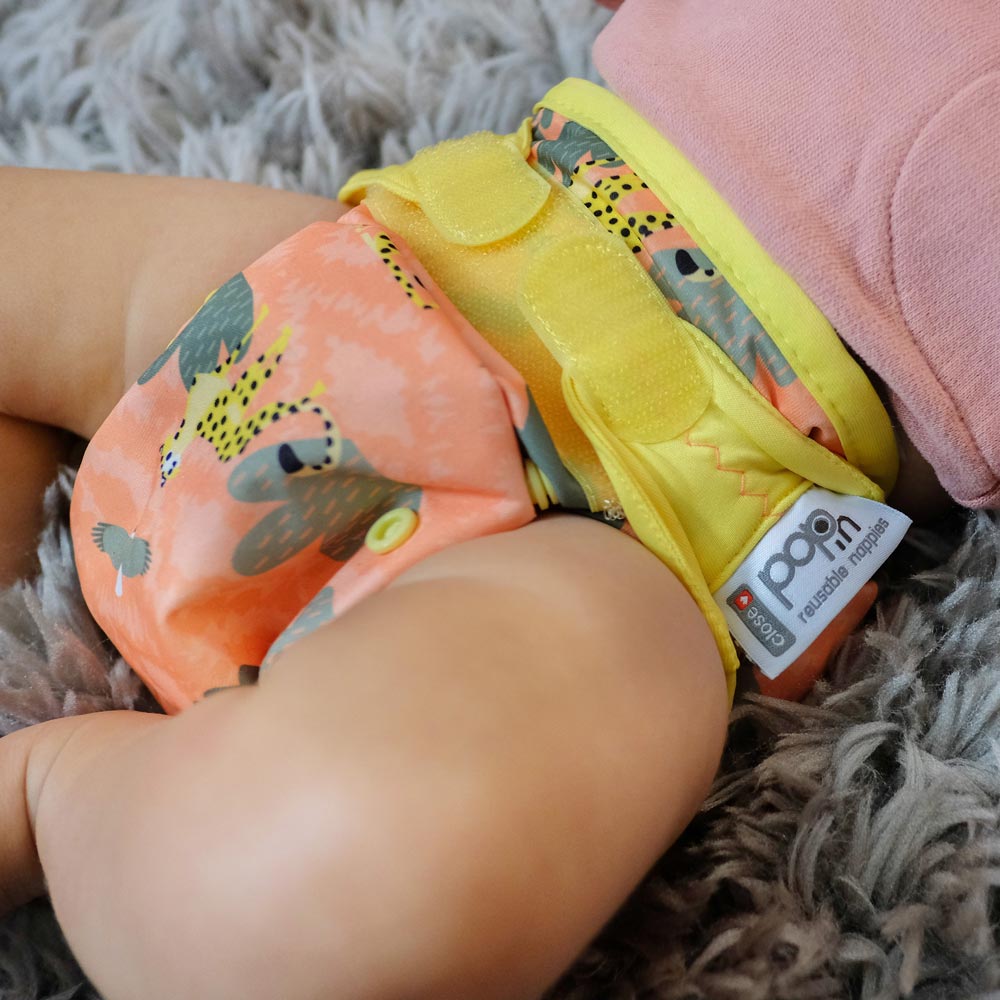 A baby wearing The Close Parent Pop-in reusable nappy wrap cover with velcro closures, in a cheetah print