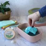 An adult's hand reaching for a wipe from the pink coloured Poppets reusable wipes container. 