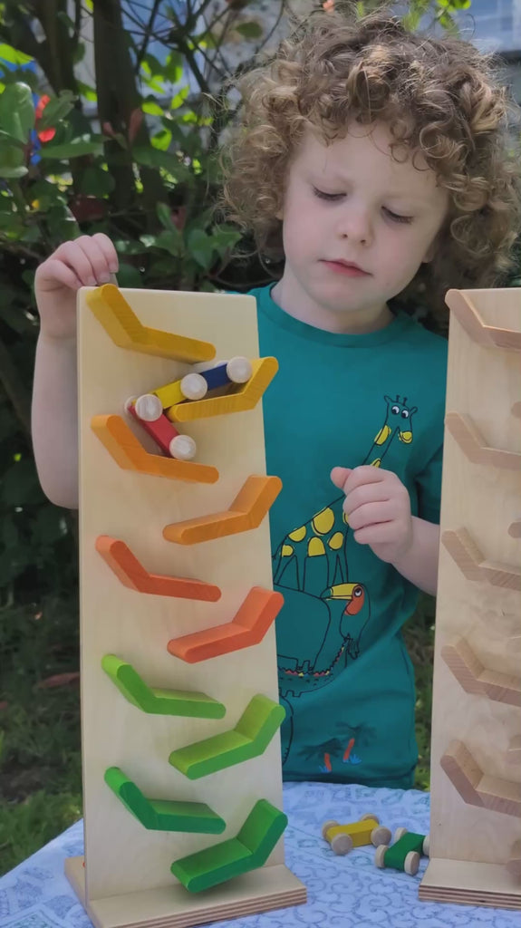 A toddler playing with the Beck Toys wooden millipede car train set in the Babipur garden. The set is a wooden plank with slats that the car train can weave down.