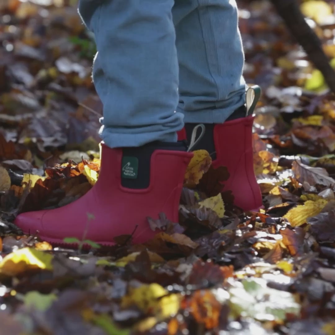 Child running through a forest wearing a pair of Little Green Radicals Ankle Wellies in Red, flexible with gripped soles, made from Fair Trade Rubber, available to buy at Babipur.