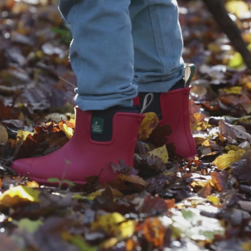 Child running through a forest wearing a pair of Little Green Radicals Ankle Wellies in Red, flexible with gripped soles, made from Fair Trade Rubber, available to buy at Babipur.