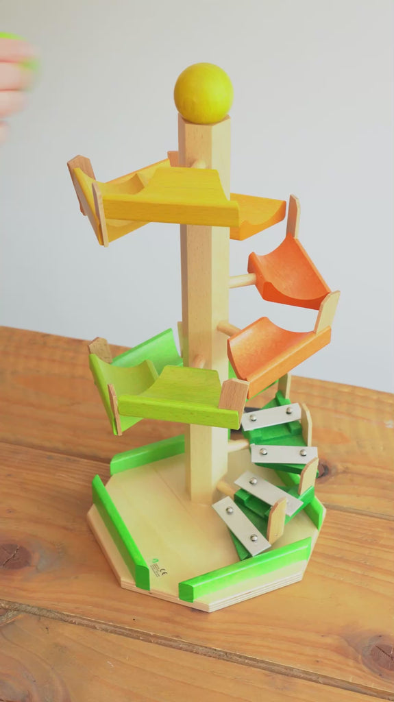 A video of the Beck Toys step tower wooden ball run in action - a woman's hand can be seen dropping large wooden balls onto the ball track, and the ball runs down in a spiral, until it reaches the xylophone notes at the bottom of the track, and plays four notes.
