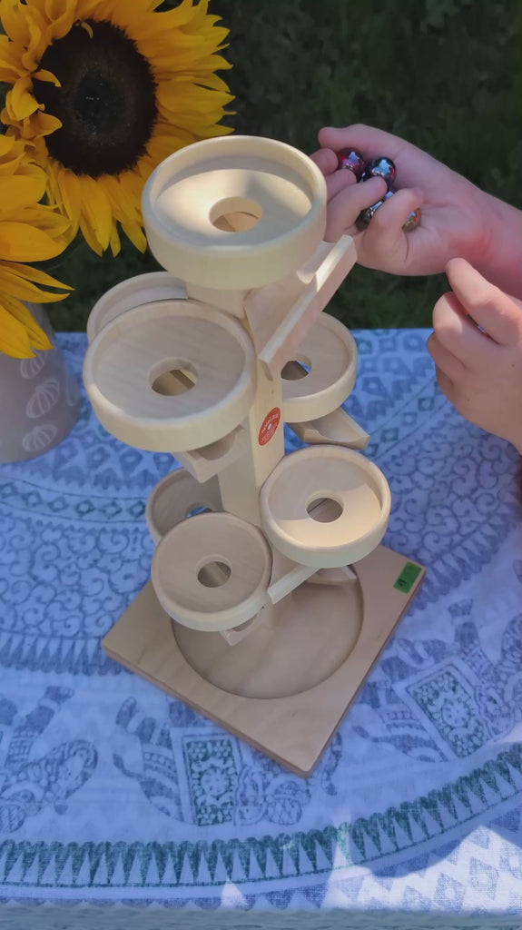 A child playing with the Beck Toys wooden plate tower marble run - it features round plates, and the marbles spin around each plate before dropping down through a hole, and rolling to the next plate. 