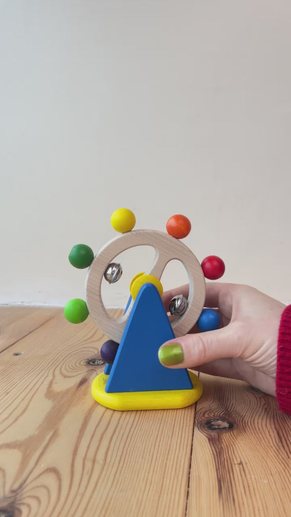 Video demonstration of Nic Ferris Wheel, a baby wooden sensory toy, a chunky bright blue stand holding a rotating wheel dotted with rainbow coloured beads and bells, for sale at Babipur.
