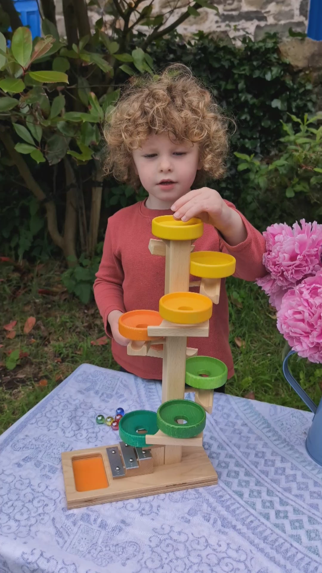 child playing with the Beck wooden marble run with xylophone at the end. Balls fall and the spin around a number of wooden pieces, then drop onto a xylophone. 