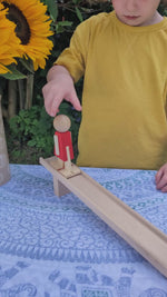 Two children playing with the Becki wooden Nurmi Ramp Walker toy, a red wooden figure that walks down a ramp on its own when pushed.