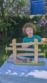 A child playing with the Beck oys wooden musical ball run track outside in the Babipur garden. The ball track allows the balls to run down in zig zag lines, hitting four xylophone nots at the bottom to create a tinkling noise.