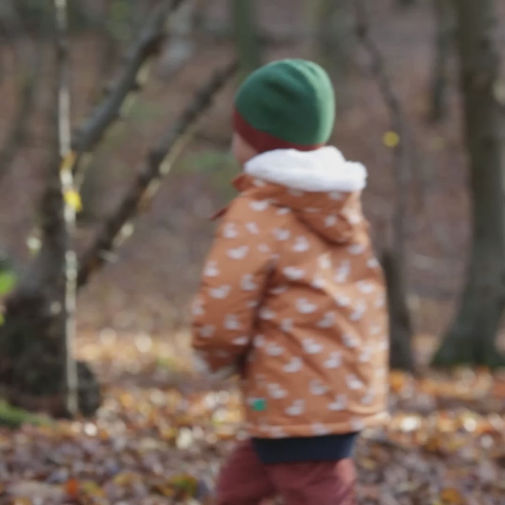 Boy running around a forest wearing a Little Green Radicals Kids Warm Waterproof Winter School Coat in a gold yellow duck print, with a cosy lined hood, for sale at Babipur.