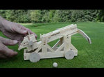 A person's hands wind up the completed Ballista model, insert a wooden ball, and fire it
