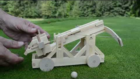 A person's hands wind up the completed Ballista model, insert a wooden ball, and fire it