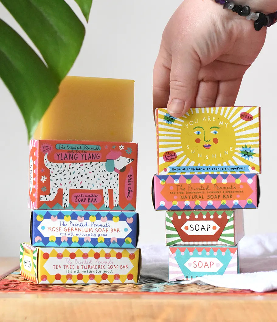 A hand reaching for the you are my sunshine illustrated soap bar box placed in a stack with other Printed Peanut natural soaps.