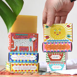 A hand reaching for the you are my sunshine illustrated soap bar box placed in a stack with other Printed Peanut natural soaps.