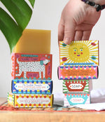 A hand reaching for the you are my sunshine illustrated soap bar box placed in a stack with other Printed Peanut natural soaps.