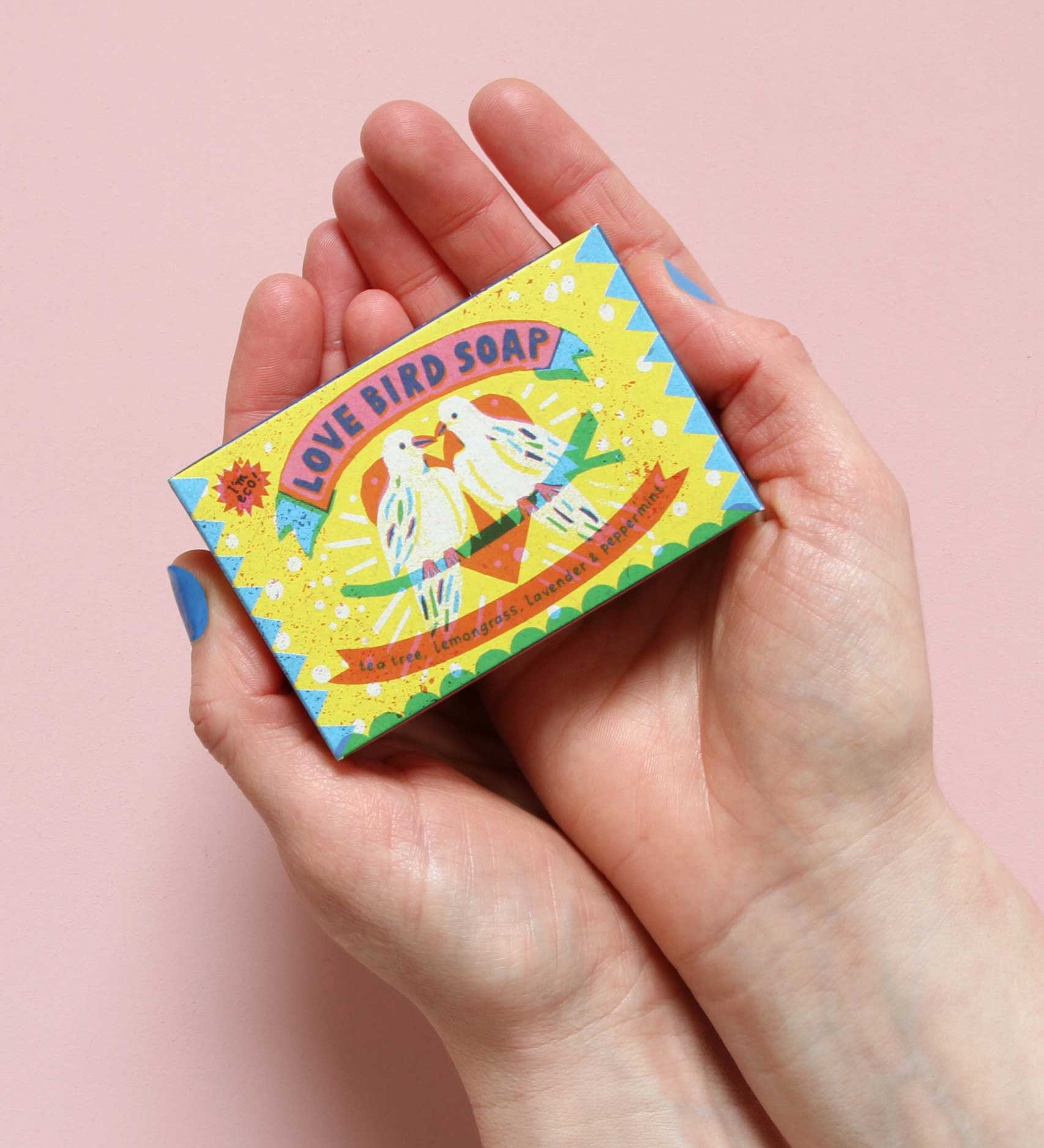 Printed Peanut love bird natural handmade soap with tea tree lemongrass lavender & peppermint. The bar is in decorative packaging in a person's hands.