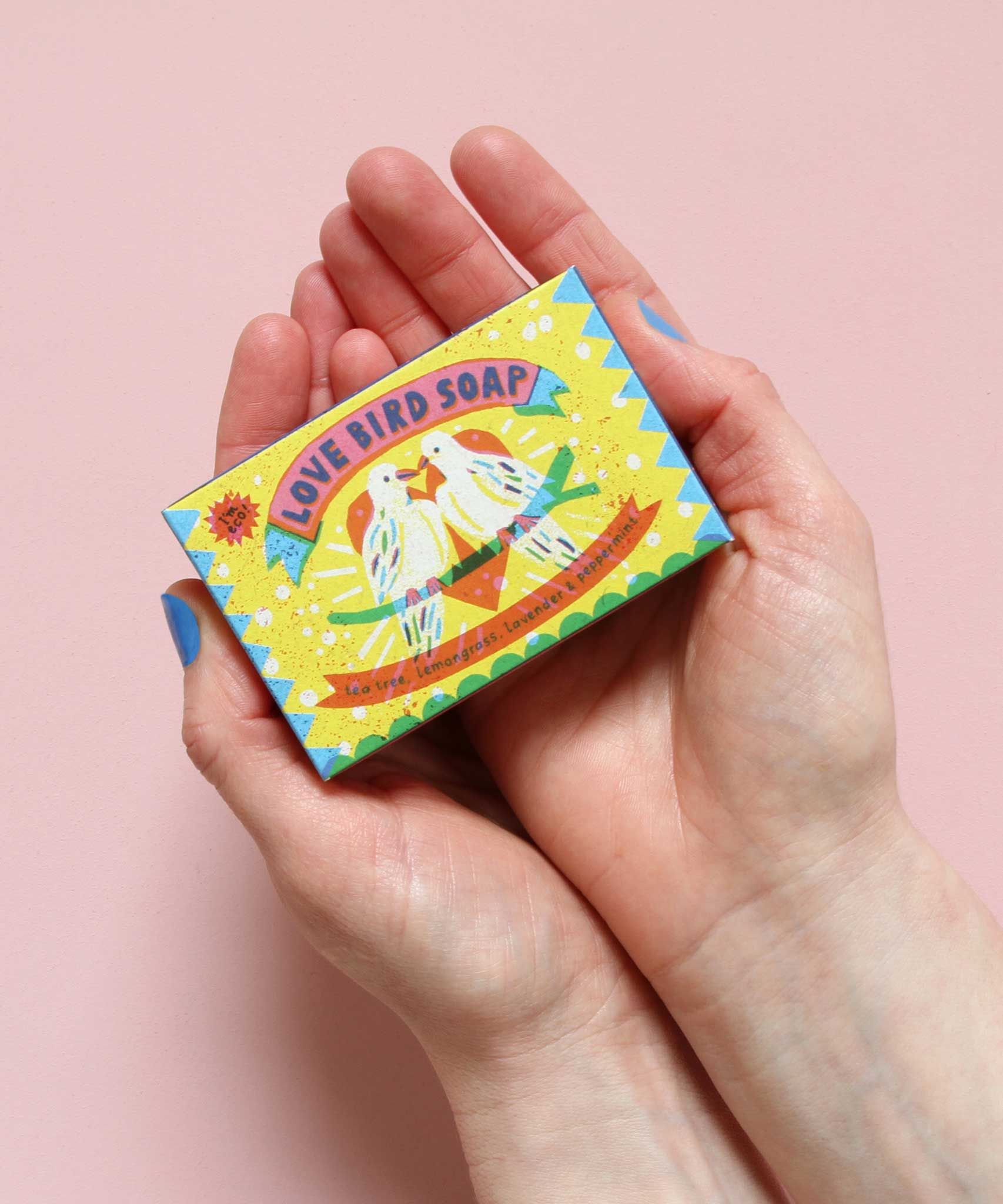 Printed Peanut love bird natural handmade soap with tea tree lemongrass lavender & peppermint. The bar is in decorative packaging in a person's hands.