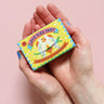 Printed Peanut love bird natural handmade soap with tea tree lemongrass lavender & peppermint. The bar is in decorative packaging in a person's hands.