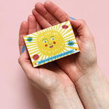 The Printed Peanut sunshine natural handmade orange and grapefruit soap. The bar is shown in a decorative packaging box placed in a person's hands. 