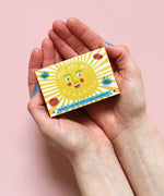 The Printed Peanut sunshine natural handmade orange and grapefruit soap. The bar is shown in a decorative packaging box placed in a person's hands. 