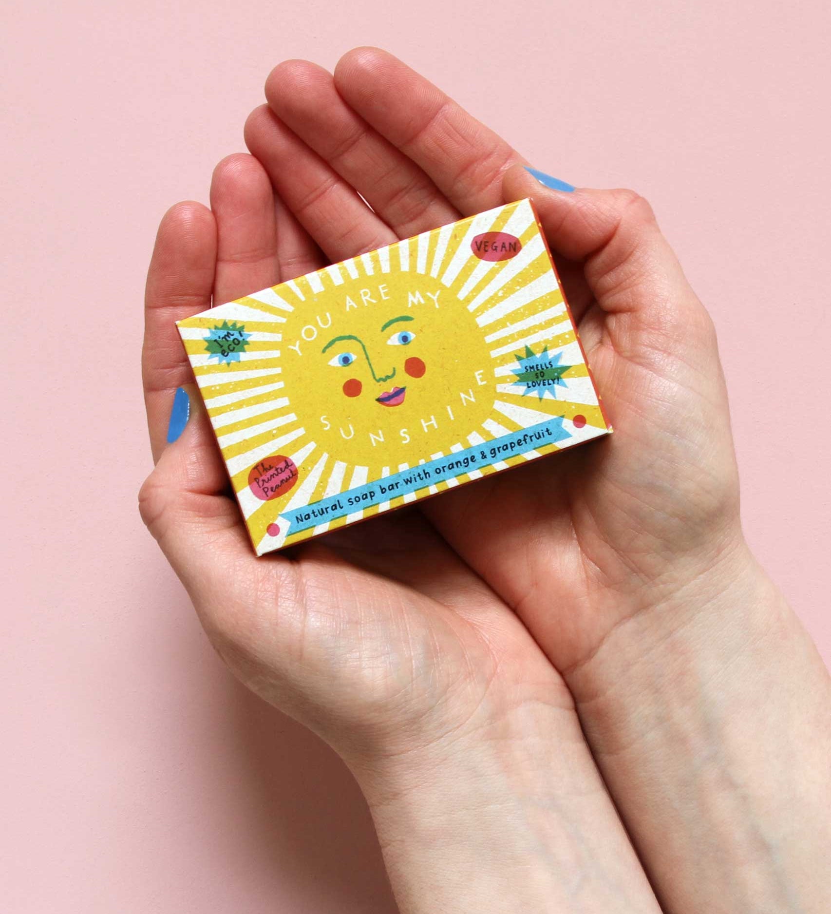 The Printed Peanut sunshine natural handmade orange and grapefruit soap. The bar is shown in a decorative packaging box placed in a person's hands. 