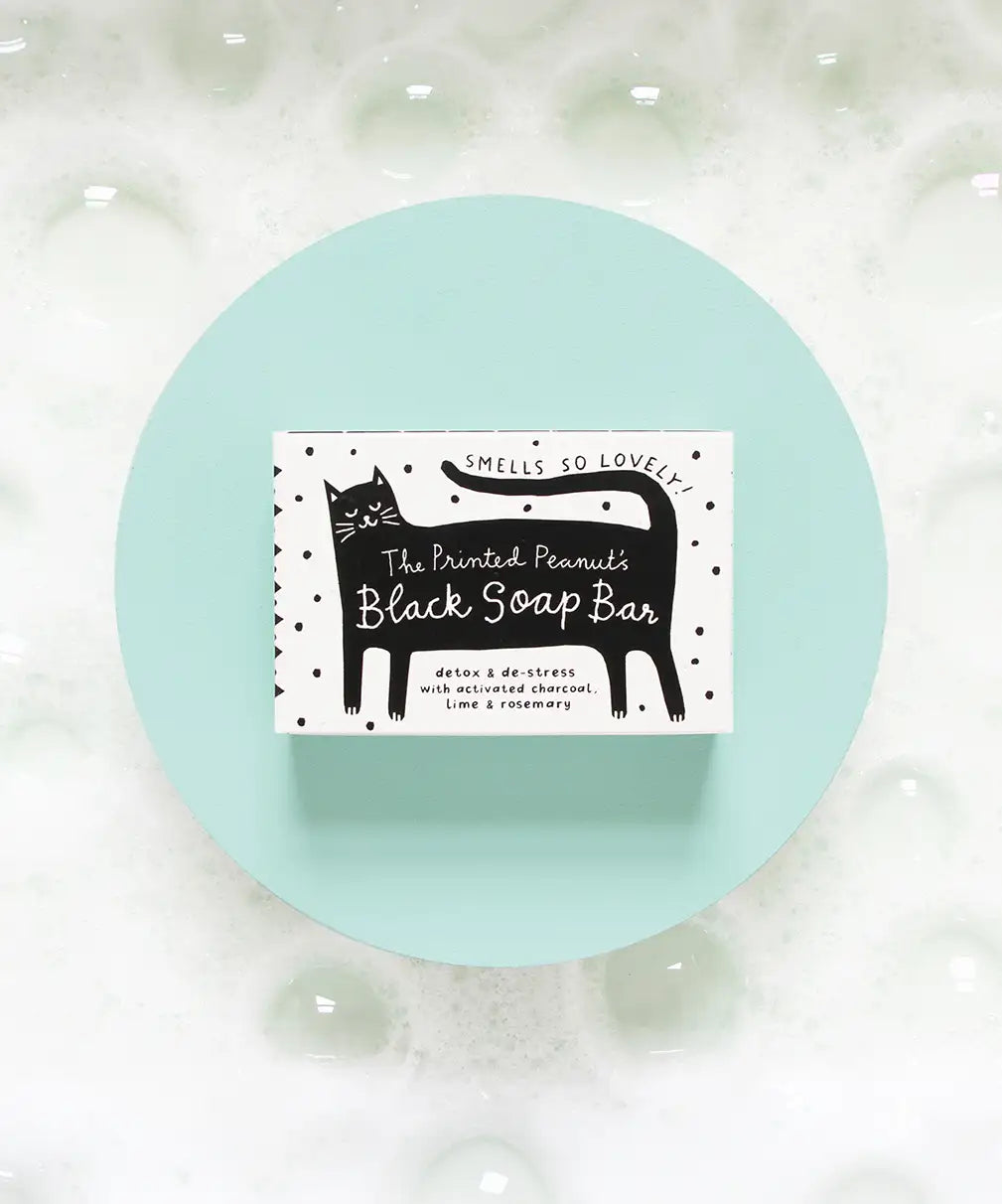 The Printed Peanut Black Cat charcoal soap gift box displayed on blue background with bubbles, natural soap with rosemary and lime.