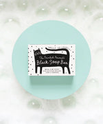 The Printed Peanut Black Cat charcoal soap gift box displayed on blue background with bubbles, natural soap with rosemary and lime.