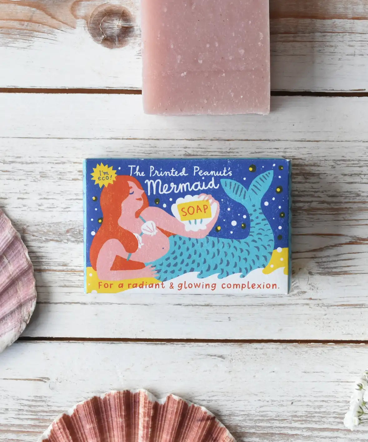 A Printed Peanut mermaid natural handmade soap bar on a wooden surface next to shells