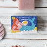 A Printed Peanut mermaid natural handmade soap bar on a wooden surface next to shells