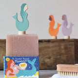 Printed Peanut rose geranium natural soap bar placed on top of the mermaid themed illustrated packaging box. Grimm's mermaid decorative figure has been placed on top. 