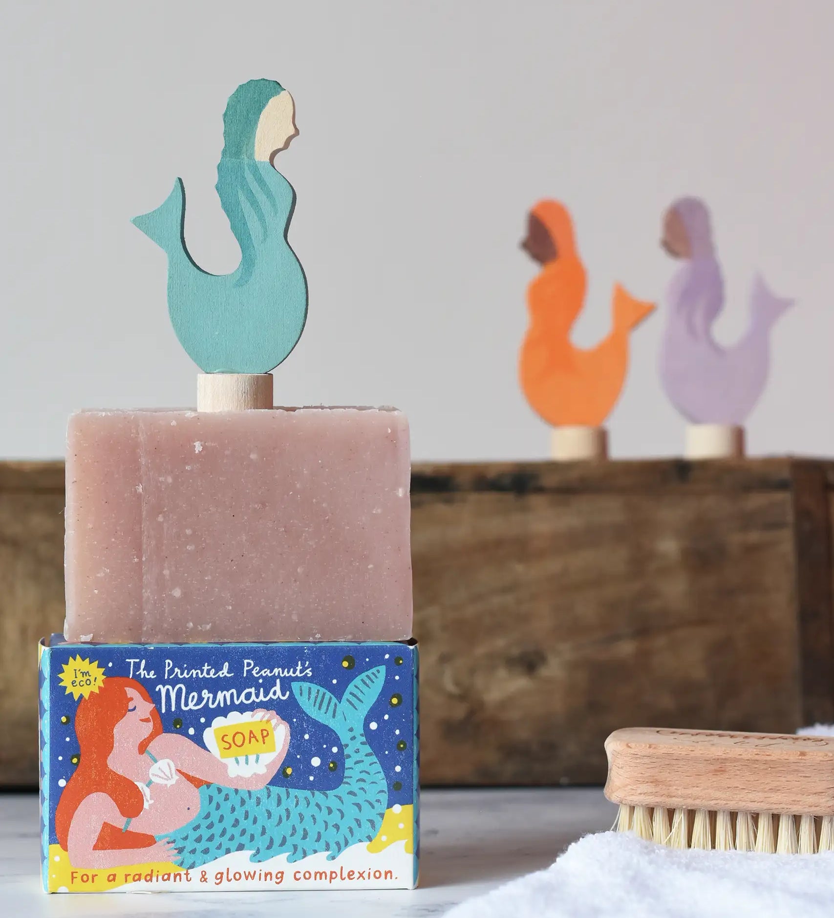 Printed Peanut rose geranium natural soap bar placed on top of the mermaid themed illustrated packaging box. Grimm's mermaid decorative figure has been placed on top. 