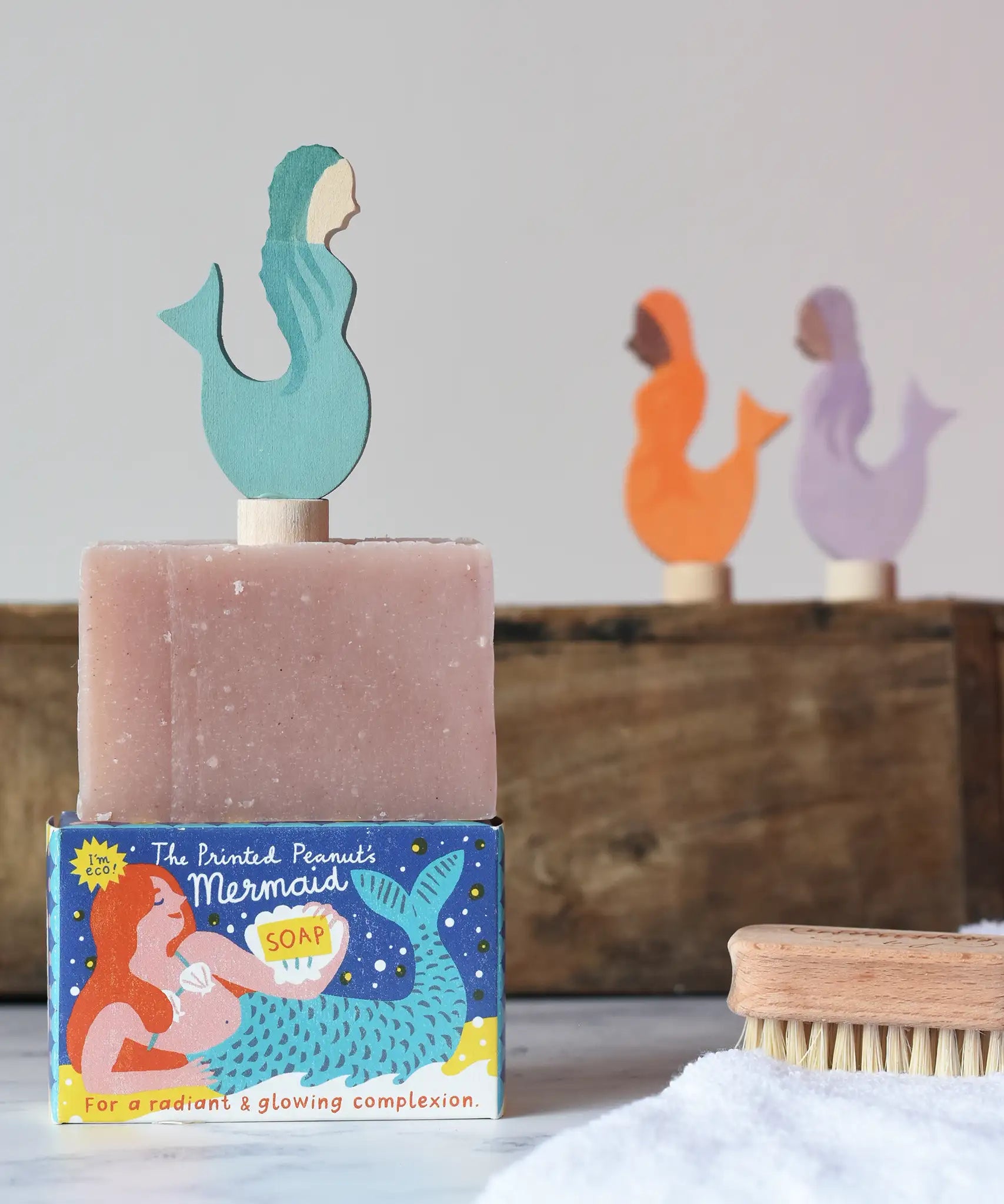 Printed Peanut rose geranium natural soap bar placed on top of the mermaid themed illustrated packaging box. Grimm's mermaid decorative figure has been placed on top. 
