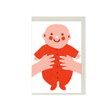 Illustrated new baby greeting card with smiling baby in red outfit, held by hands, mini A7 baby gift card by The Printed Peanut
