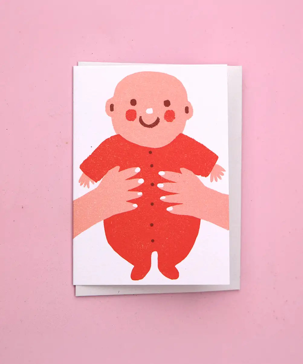 The Printed Peanut new baby greeting card with baby in red outfit, illustrated mini new baby card displayed on pink background