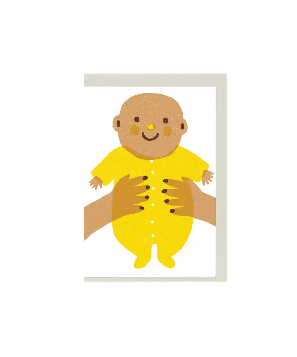 Illustrated new baby greeting card with smiling baby in yellow outfit, held by hands, mini A7 gift card by The Printed Peanut