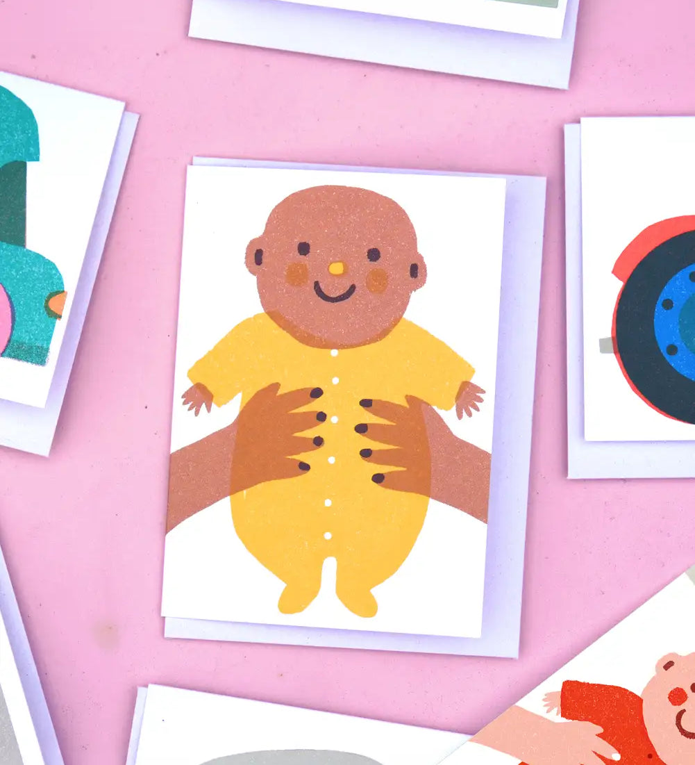 The Printed Peanut new baby greeting card with baby in yellow outfit, displayed with other illustrated mini gift cards on pink background