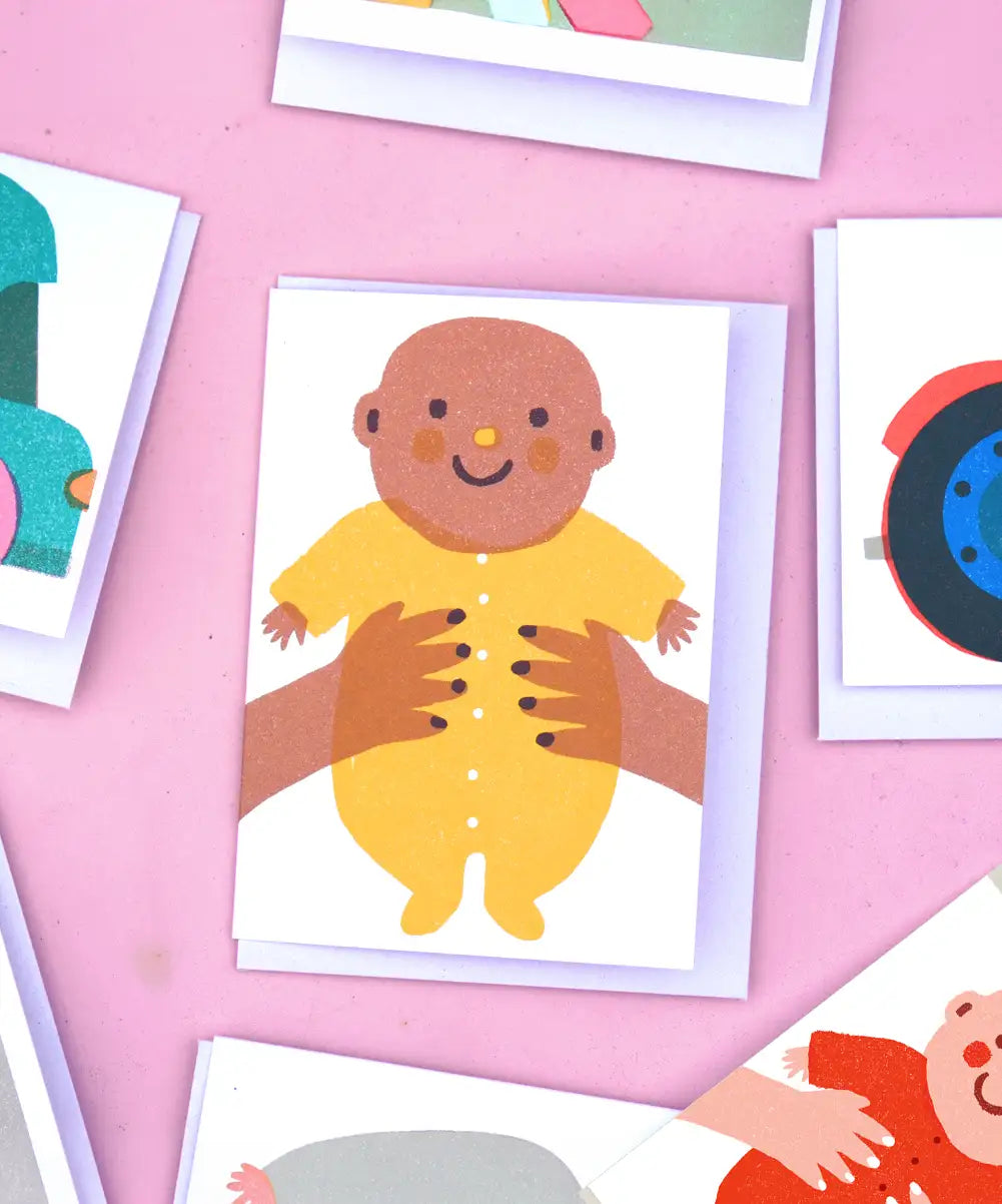 The Printed Peanut new baby greeting card with baby in yellow outfit, displayed with other illustrated mini gift cards on pink background