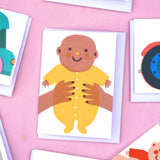 The Printed Peanut new baby greeting card with baby in yellow outfit, displayed with other illustrated mini gift cards on pink background