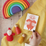 The Printed Peanut red new baby mini greetings card shown in an adult's hand surrounded by wooden toys in the Babipur playroom.