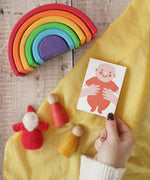 The Printed Peanut red new baby mini greetings card shown in an adult's hand surrounded by wooden toys in the Babipur playroom.