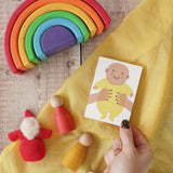 The Printed Peanut yellow new baby mini greetings card shown in an adult's hand surrounded by wooden toys in the Babipur playroom.