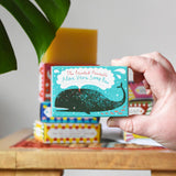 Close up of the Printed Peanut aloe vera fragrance free natural handmade soap bar in a decorative blue cardboard box showing a whale illustration in an adult's hand.