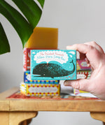 Close up of the Printed Peanut aloe vera fragrance free natural handmade soap bar in a decorative blue cardboard box showing a whale illustration in an adult's hand.
