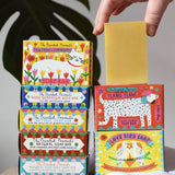 A stack of Printed Peanut soap bars in their illustrated cardboard packaging boxes. One natural soap bar has been taken out of it's packaging.