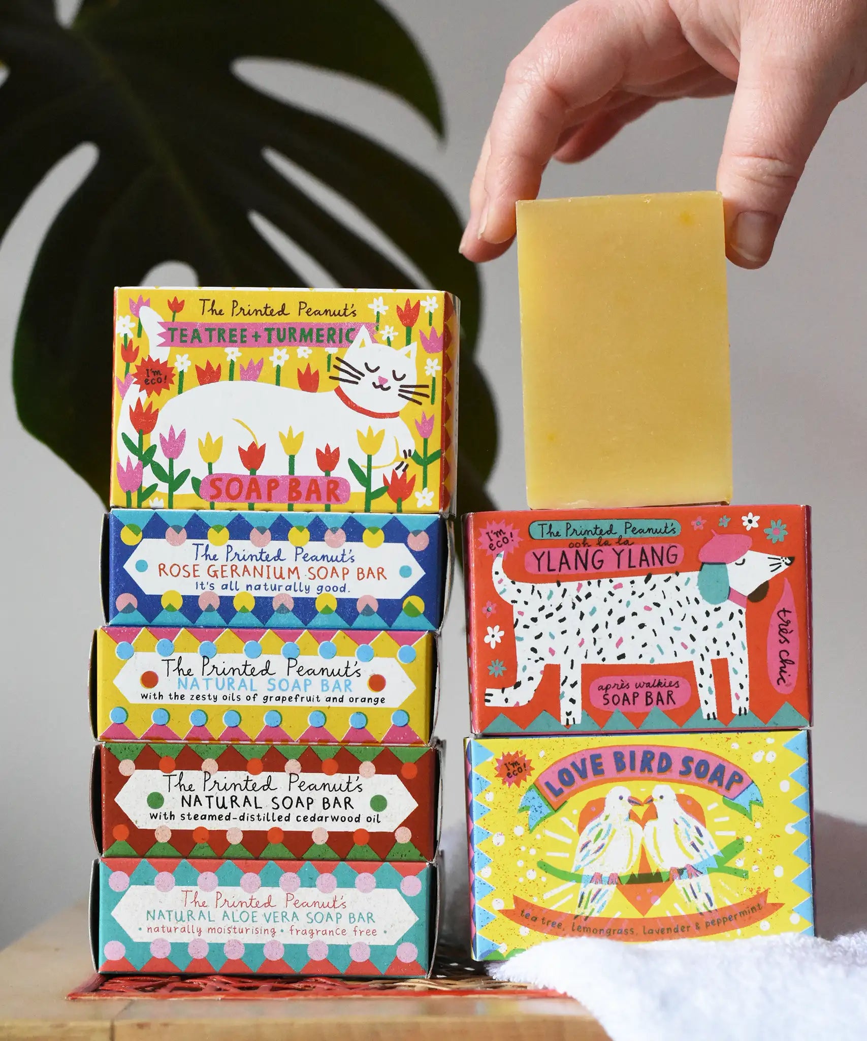 A stack of Printed Peanut soap bars in their illustrated cardboard packaging boxes. One natural soap bar has been taken out of it's packaging.