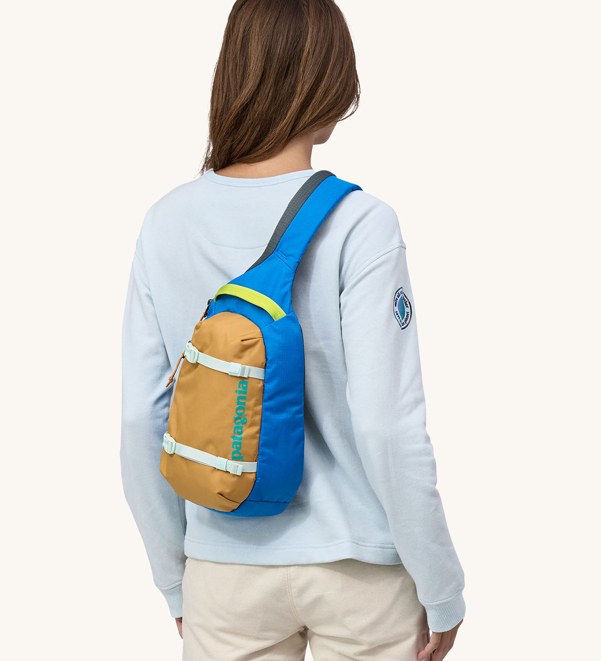An adult wearing the Patagonia Atom Sling 8L - Patchwork bag in Vessel Blue on their shoulder