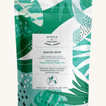 White with green leaves queasy tea pouch on a cream background.