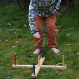 A child kneeling, playing with the Wooden Story Ring Toss Game. One of the hoops can be see mid-air about to land on one of the coloured wooden posts.
