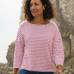 A woman standing outside wearing the Rapanui striped boat neck t-shirt in redwood stripe design. A organic cotton long sleeve top in a relaxed fit style with white and red stripes