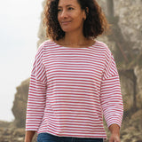 A woman standing outside wearing the Rapanui striped boat neck t-shirt in redwood stripe design. A organic cotton long sleeve top in a relaxed fit style with white and red stripes